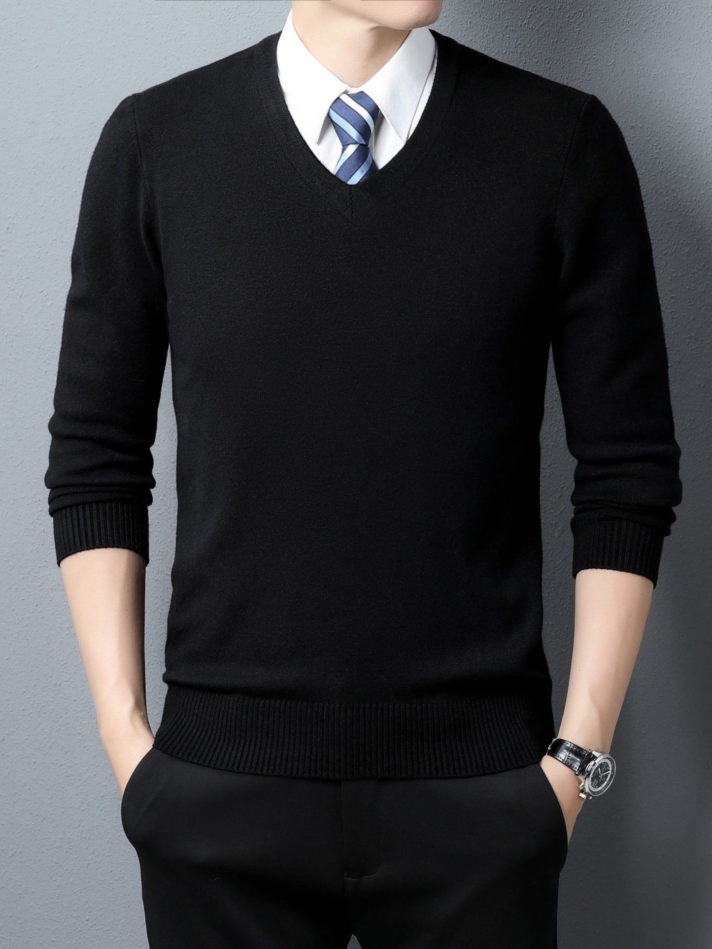 Person wearing a black Men's Knitted V-neck Sweater over a white shirt with a blue striped tie against a gray background