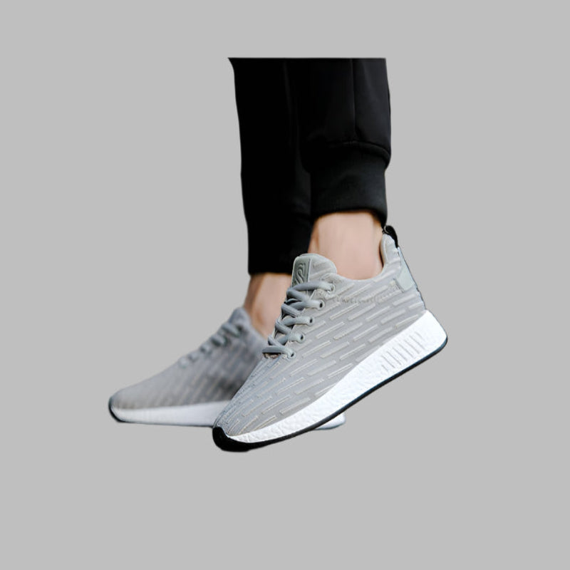 Gray sneakers worn with black pants on a gray background
