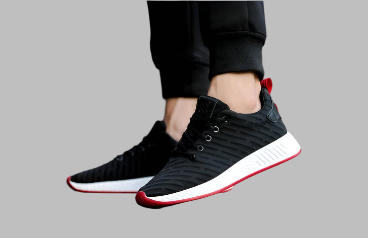 Black sneakers with red accents worn by a person on a gray background