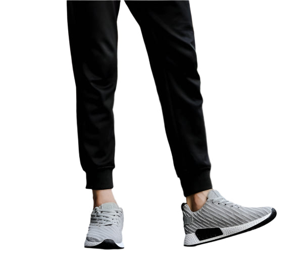 Gray athletic shoes worn with black pants on a white background