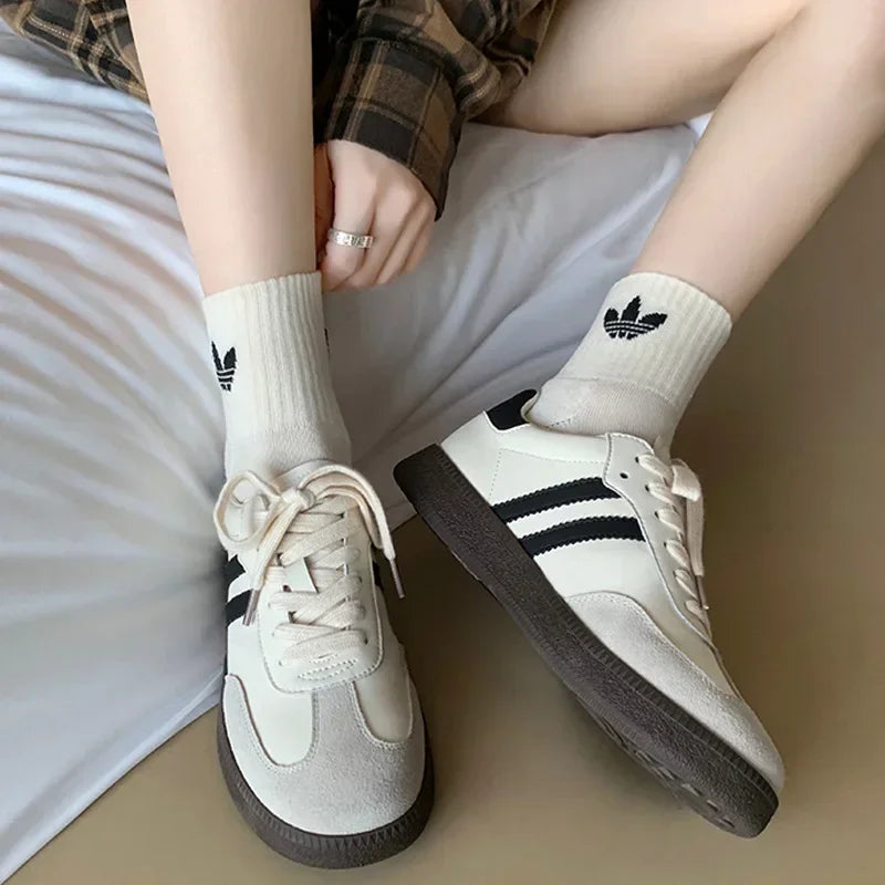 White sneakers with black stripes and Adidas logo on socks, sitting on a white surface.