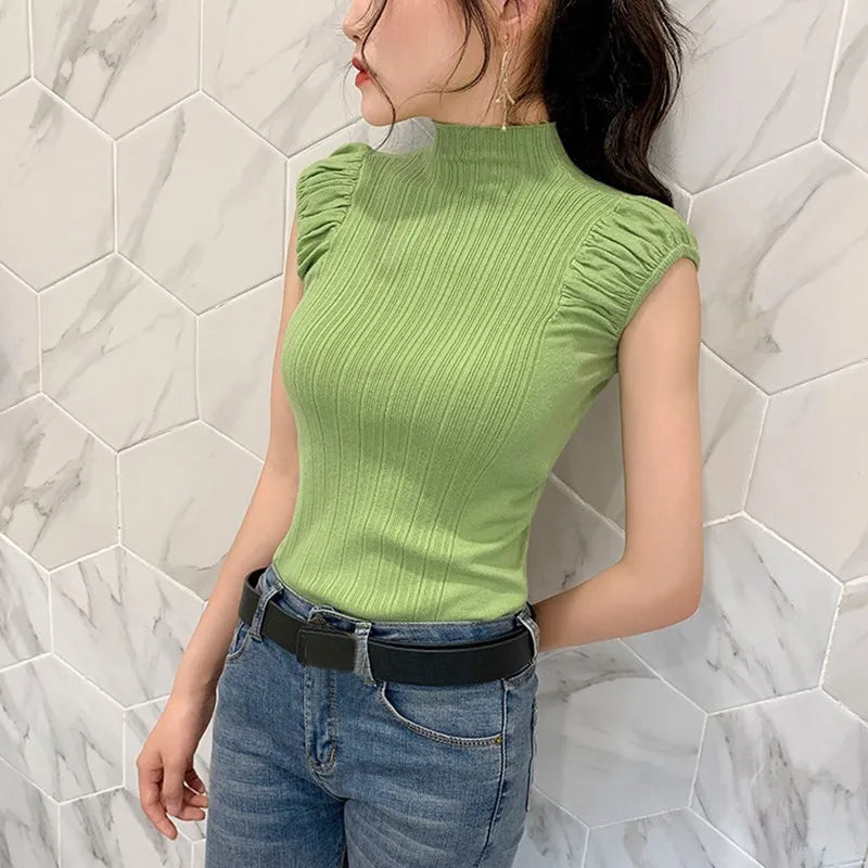 Person wearing a green ribbed top and blue jeans against a marble wall.