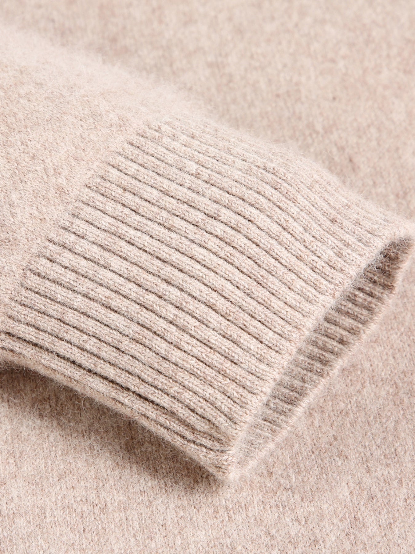 Close-up of a beige knitted sweater sleeve on a matching fabric background